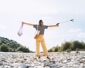 Person help to keep nature clean up and pick up garbage. Young woman clean up outdoor area from rubbish. Volunteer female collecting plastic waste trash on stones of river beach.