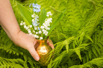 Lilies of the valley in May and forget-me-nots in a charming little jug held in a woman's hand...