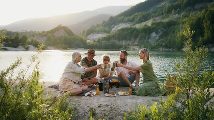 Happy multigeneration family on summer holiday trip, barbecue by lake.