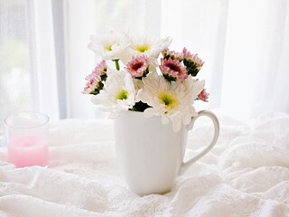 White pink flowers in mug cup of tea on embroidered cloth lace, window soft light background...