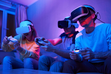 Friends playing virtual reality games using joysticks while sitting on the couch.