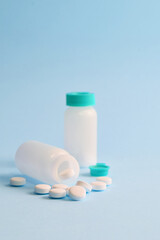 Close up, white round tablets and small bottle on light blue background.