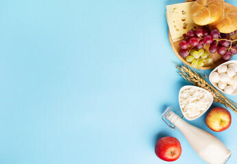 Jewish Shavuot holiday card concept. Dairy products, fruits, cheese, bread, milk bottle on blue...