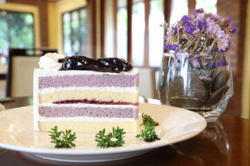 Close up blueberry sponge layer cake topping by blueberry sauce on white plate on wooden table in...