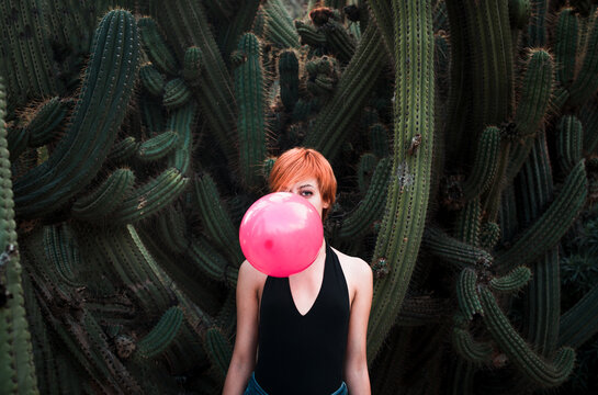 Woman hiding behind balloon surrounded by cactus 