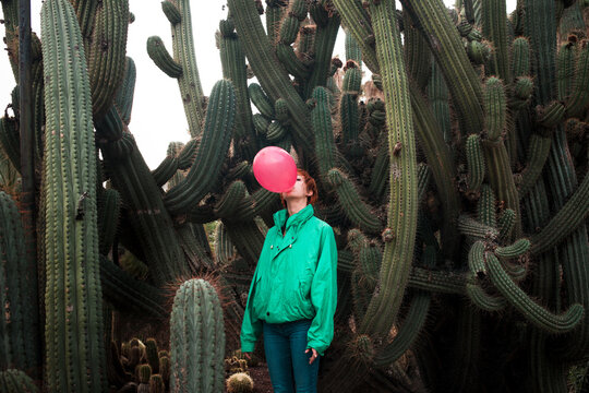 Optimistic woman with pink balloon surrounded by cactus
