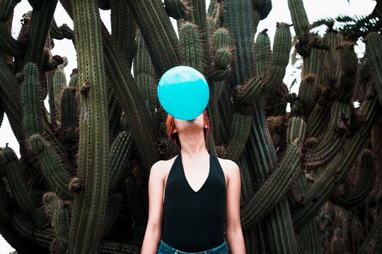 Conceptual portrait of woman blowing ballon with cactus background 