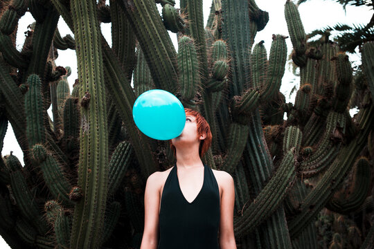 Woman inflating a balloon surrounded by cactus