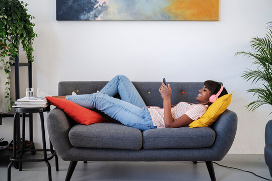 Female meloman using smartphone and resting on couch
