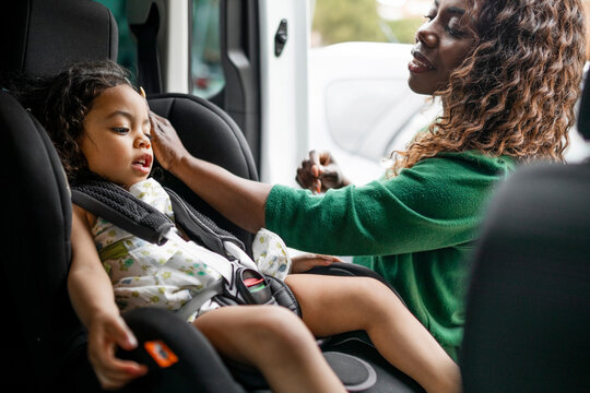 Young black mother putting daughter in car seat