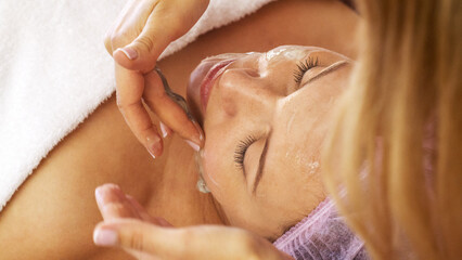 Woman in a spa salon on cosmetic procedures for facial care. Cosmetologist applies  a cosmetic...