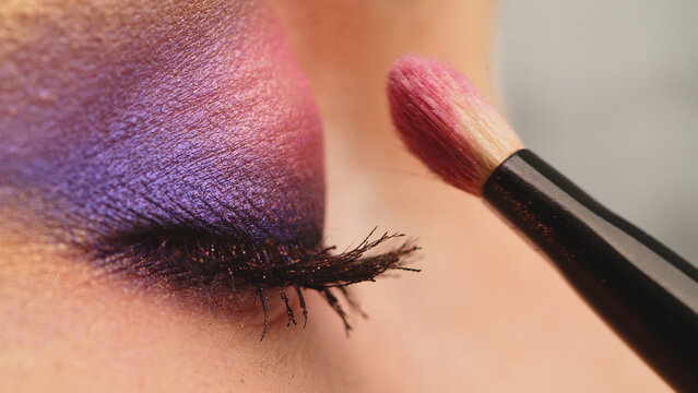 Make-up artist applies makeup to the upper eyelid, close-up.  Makeup artist applies a bright eye shadow with a makeup brush. Tutorial master class of professional makeup.