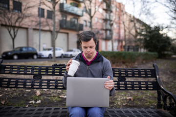 Young man with down syndrome with a laptop in a park