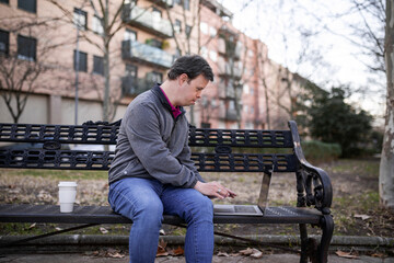 Young man with down syndrome with a laptop in a park