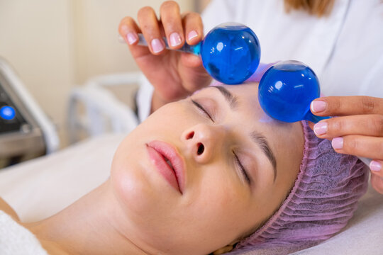 Beautician making a massage of the  face using the blue balls. Woman in a spa salon on cosmetic procedures for facial care. Girl gets massage of a face. Cosmetologist makes face massage.