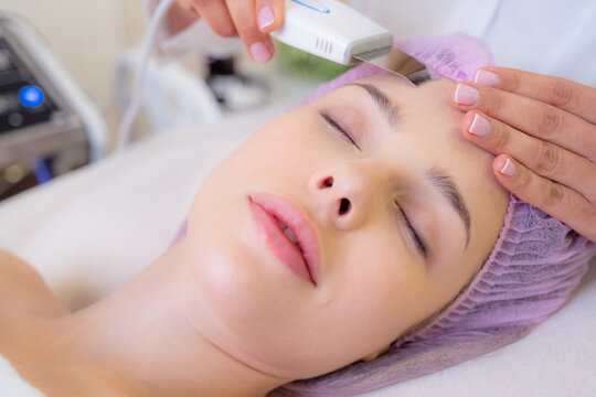 Woman in a spa salon on cosmetic procedures for facial care. Cosmetologist making a woman a therapeutic procedure on a face. Beautician makes medical procedures using a professional  equipment.