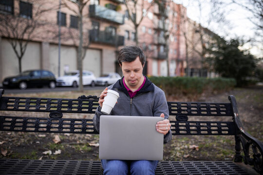 Young man with down syndrome with a laptop in a park