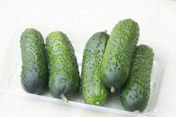 Green cucumbers in a plastic box with water drops on a light table