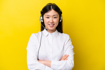 Telemarketer Chinese woman working with a headset isolated on yellow background keeping the arms...