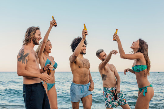 Multi-ethnic friends having fun at the beach and drinking beer