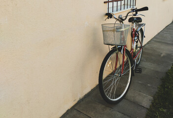 Fototapeta na wymiar A red bicycle with a basket stands against a beige wall