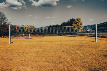 a volleyball court in a park with yellow grass. a volleyball net on drying grass field. landscape of a public park with a dramatic sky
