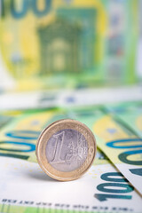 One euro coin standing on the one hundred euro banknotes