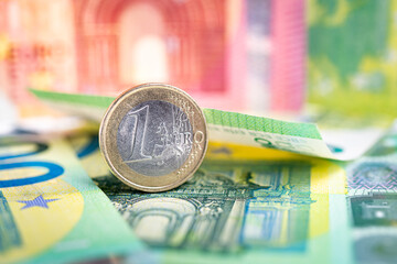 One euro coin standing on one hundred euro banknotes. European currency concept with red and green banknotes in the background.