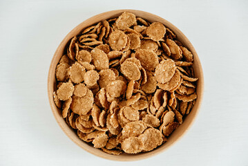 Crispy healthy dry cereal flakes in a wooden bowl on white background