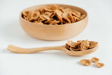 Crispy healthy dry cereal flakes in a wooden bowl with wooden spoon on white background