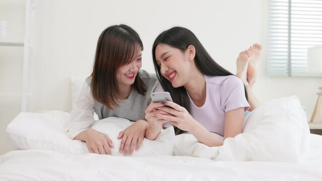 couple young asian woman are looking at mobile phone together. they are watching on cell phone with happy emotion..