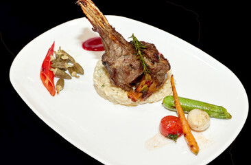 Rack of lamb. Fried or baked meat with vegetables in a plate on a black background.