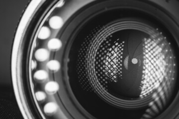 Professional camera photo lens. Details of glass, layer of enlightenment, aperture petals. Light reflections from modern diode lamps. The concept of making visual content. Black and white.