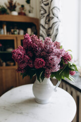 a bouquet of lilacs in a white vase on the table. lilac branches in a ceramic vase on a white table in the kitchen. a fresh bouquet of lilac decorates the kitchen room