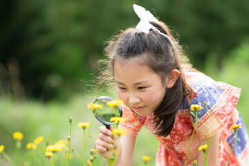 虫眼鏡で花を見る少女 - obrazy, fototapety, plakaty