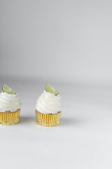 Lime cupcake on a plate with other cupcakes and a margarita in the background, lime cupcake with white buttercream and a a lime wedge, margarita cupcake
