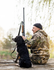 Male hunter sitting on a bridge against the backdrop of sunrise and forest with a lake with a...