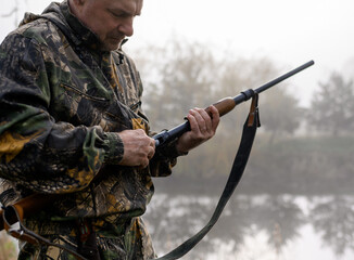 Hunter charges a cartridge into the chamber of a rifle close up on a background of reeds