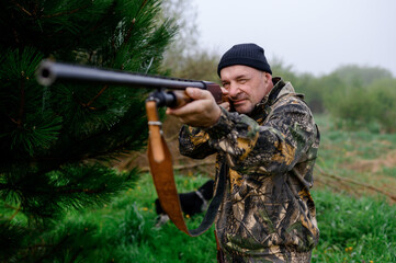 Hunter aims a gun against the backdrop of a misty lake and picea with his dog Russian Spaniel