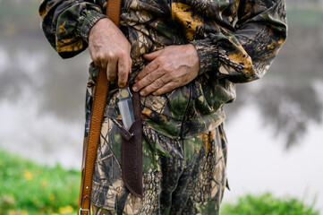 Hunter's hand with a knife on a background of guns and a lake in the fog