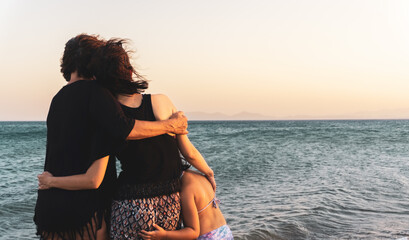 Grandmother, mother and daughter hugging each other, looking distant sea and watching sunset....