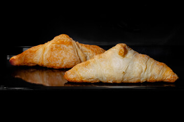 Two baked croissants on tray in electric oven - close up view, black background. French cuisine, homemade bakery, breakfast, food, cooking and pastry concept