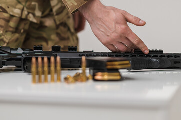 A military man takes a machine gun from the table. Machine gun with cartridges on a white table