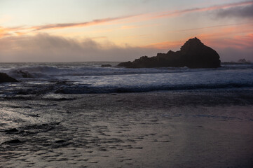 Fototapeta na wymiar Tidal waves flowing out at Pfeiffer beach, while it is enshrouded by a purble sunset color.