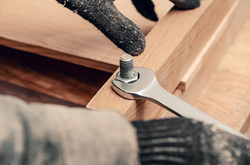 Male hands tighten the nut on the thread of the bolt screwed into the wooden structure.