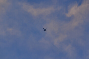 jet plane silhouette flying at high altitude crossing the blue sky covered by a sky of white clouds.