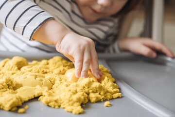 Obraz na płótnie Canvas Hands of child moulding with magic kinetic sand. Cute little boy playing with kinetic sand. Development of fine motor skills. Early sensory education. Sand art therapy. Activities Montessori.