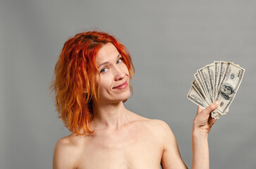 Naked woman with money. Red hair, blue eyes. She holds a fan of $ 100 bills near her face.