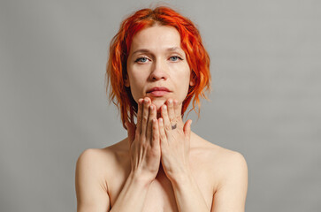 Redhead naked woman. Hands near the face.Blue eyes. Gray background.