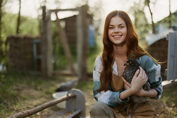 Young woman smiling for the camera holding a chicken and happy working on the farm